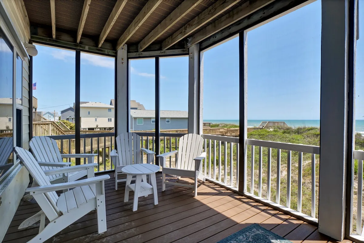 A serene screened-in porch with Adirondack chairs facing an unobstructed ocean view. The tranquil setting is ideal for morning coffee, reading, or unwinding together at the end of the day.