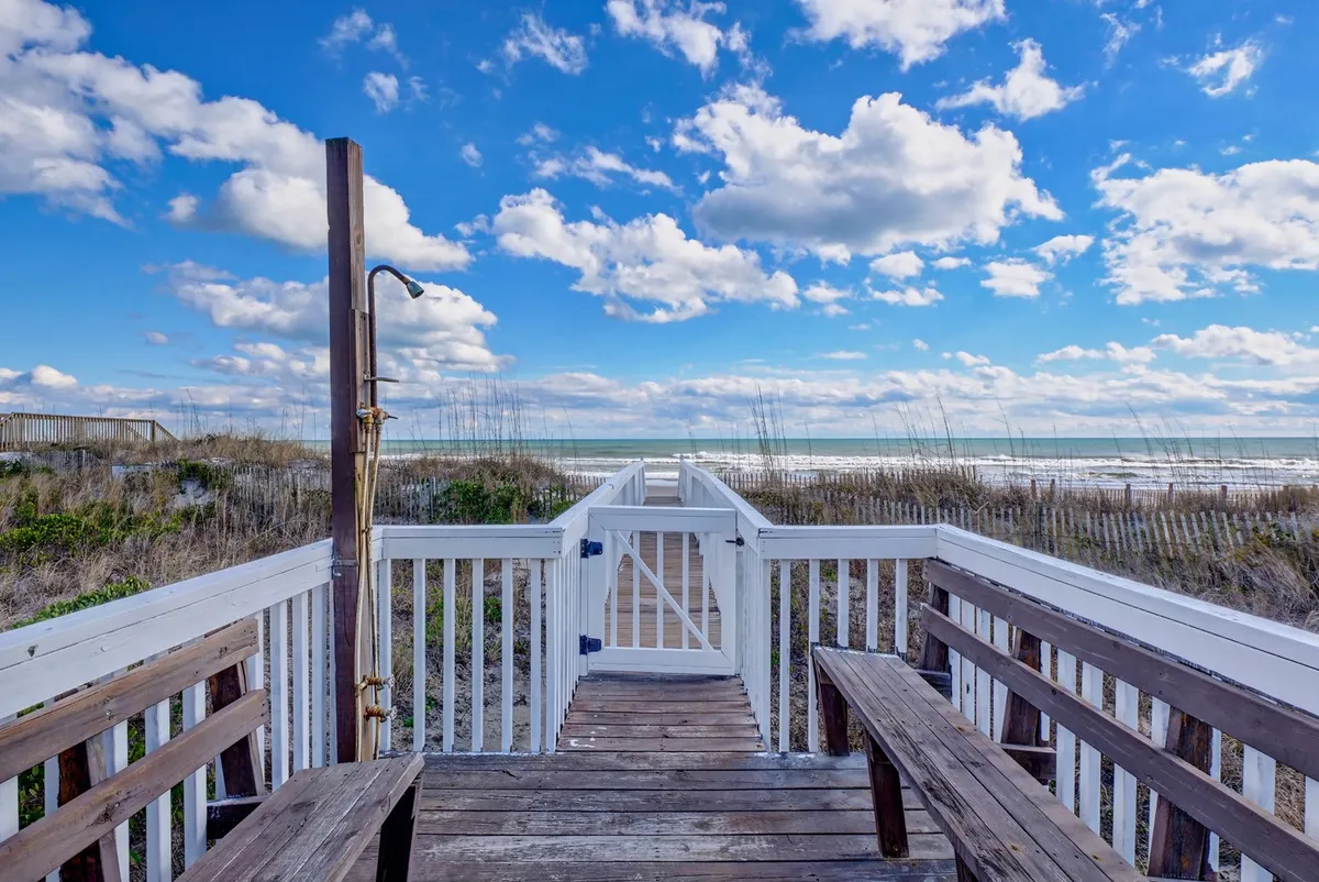 A scenic wooden walkway leading to the beach with benches, ocean waves in the background, and a cloudy sky overhead, inviting moments of strolling, unwinding, and taking in the coastal scenery.