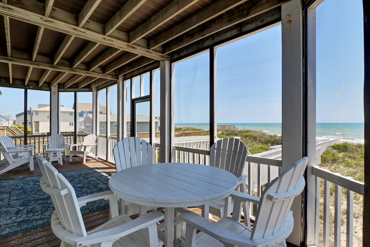 A serene outdoor area featuring white Adirondack chairs and a round table overlooking the ocean, ideal for relaxing, dining, or socializing with friends as the sun rises or sets over the water.